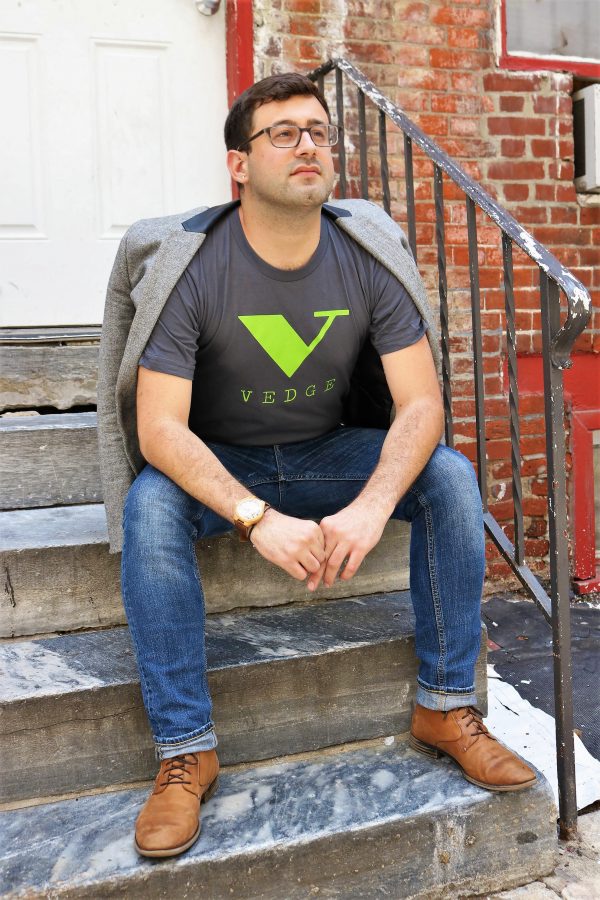 Model sitting on a stoop wearing grey t-shirt with green vedge logo