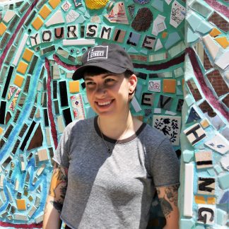 Model wearing v street hat in front of multicolor mural